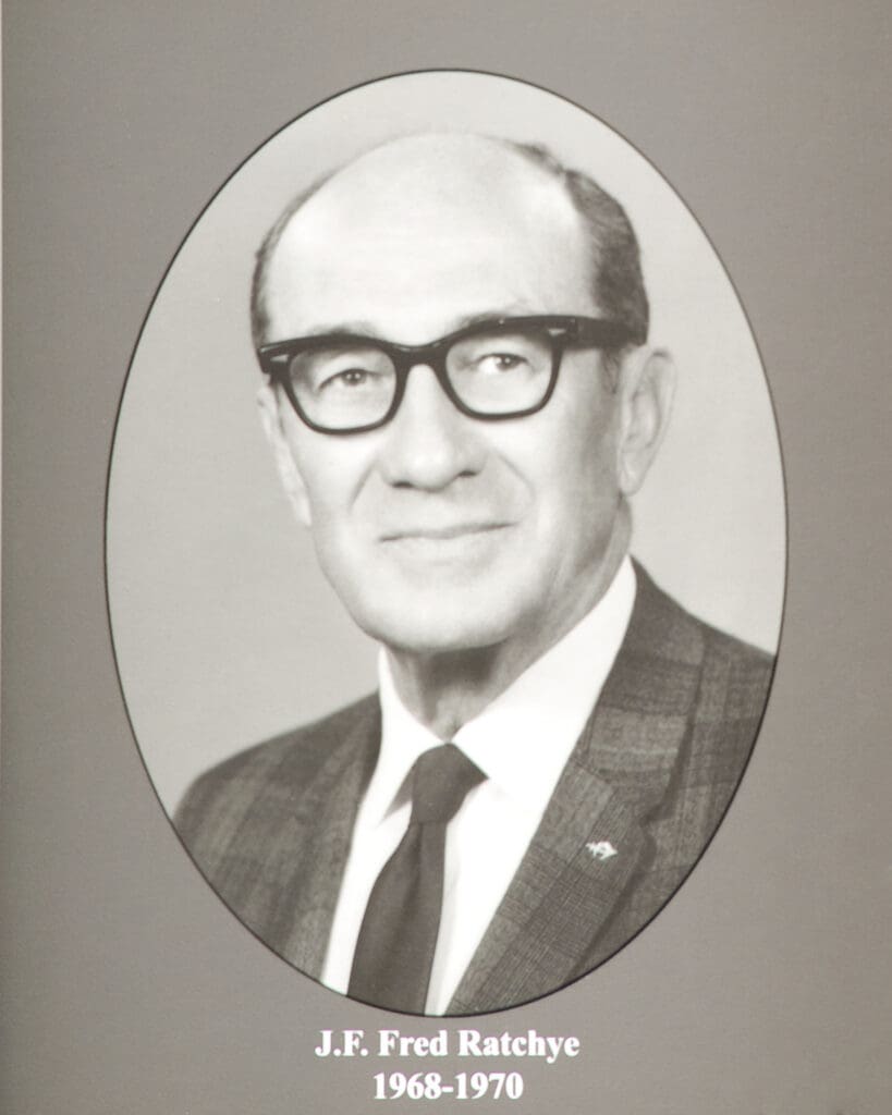 Black-and-white formal portrait of J.F. Fred Ratchye in an oval frame, wearing glasses and a suit with a tie, captioned 'J.F. Fred Ratchye 1968-1970'