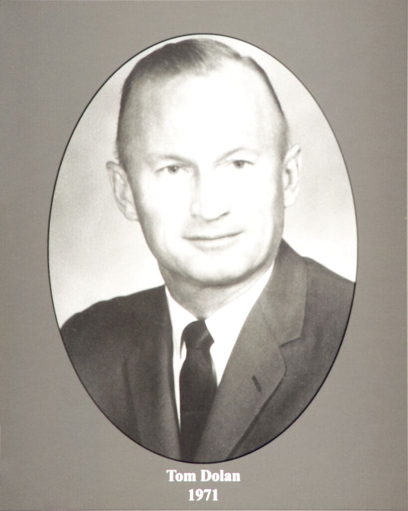 Black-and-white oval portrait of Tom Dolan in a suit, caption reads 'Tom Dolan 1971'.