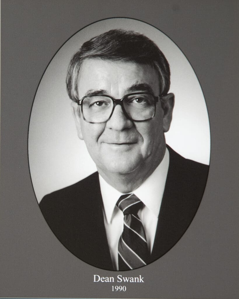 Portrait of Dean Swank in an oval frame, wearing glasses, suit, and striped tie; caption reads 'Dean Swank 1990'.