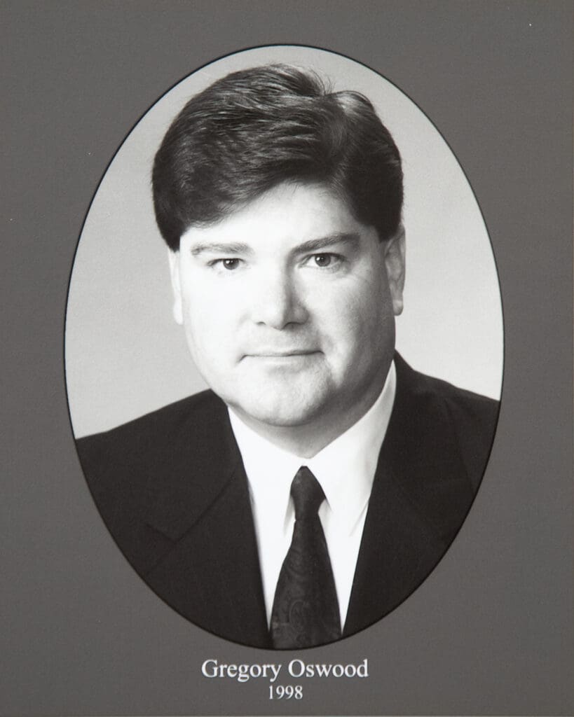 Portrait of Gregory Oswood wearing a suit and tie, in an oval-framed black-and-white photograph (1998).