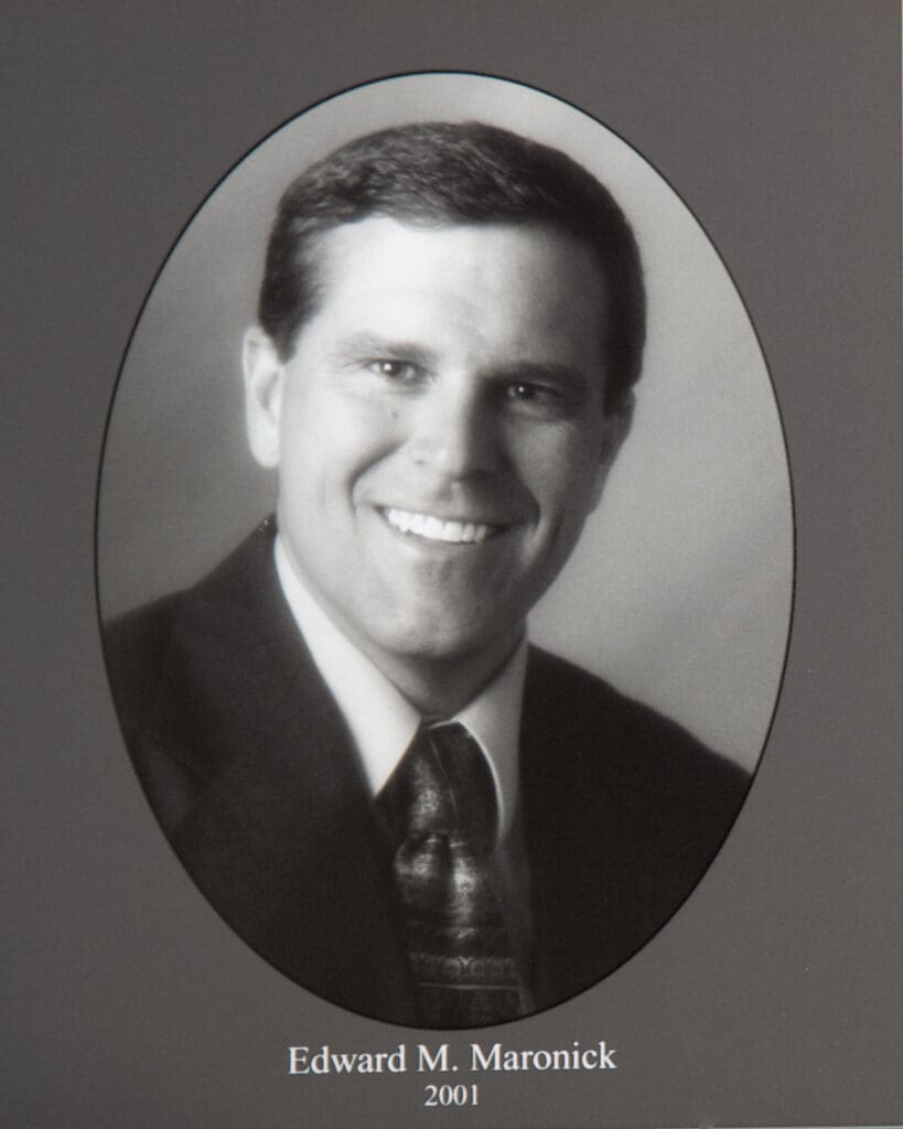Black-and-white oval portrait of a smiling man in a suit; caption reads ‘Edward M. Maronick 2001’.