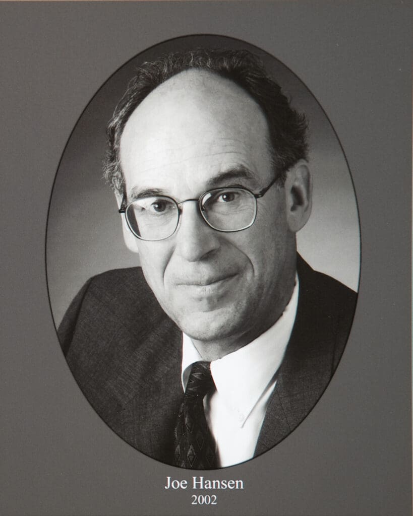 Black-and-white portrait of a man in glasses and suit, inside an oval frame; caption reads Joe Hansen 2002.