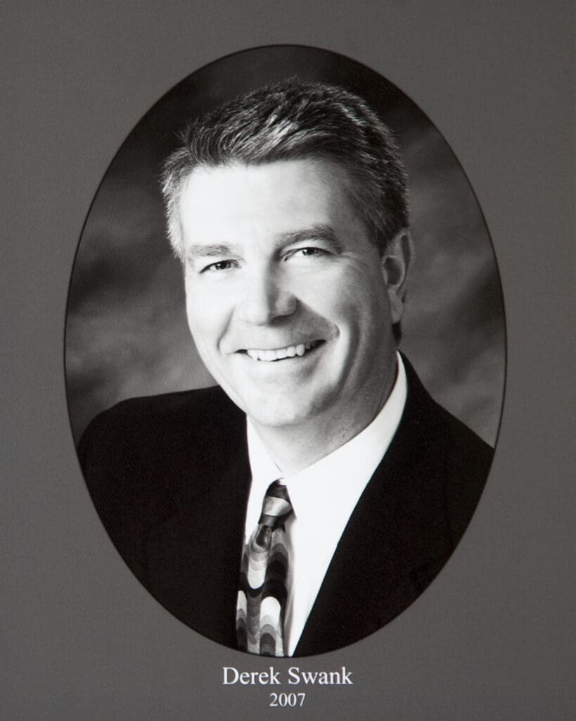 Smiling man in a suit inside a circular photo frame; caption reads Derek Swank, 2007.