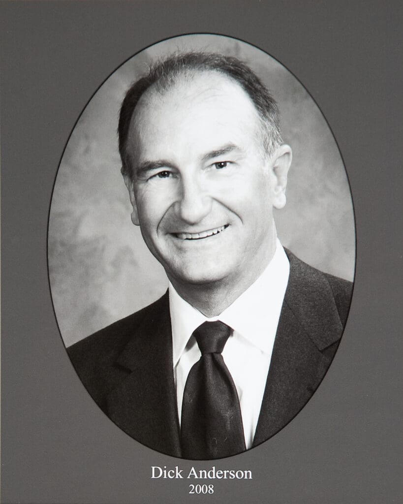 Portrait of Dick Anderson in a suit and tie, inside an oval frame on a gray background (caption: Dick Anderson, 2008).