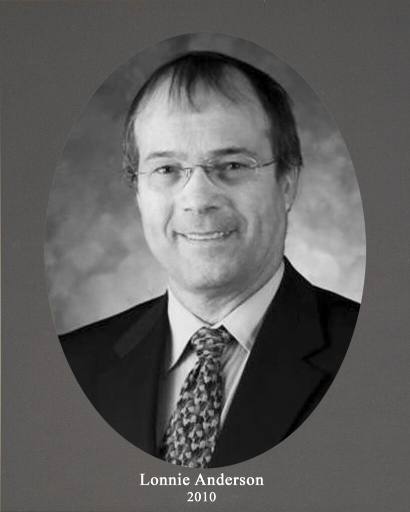 Black-and-white head-and-shoulders portrait of Lonnie Anderson in a suit and patterned tie, oval crop on gray background, caption reads ‘Lonnie Anderson 2010’