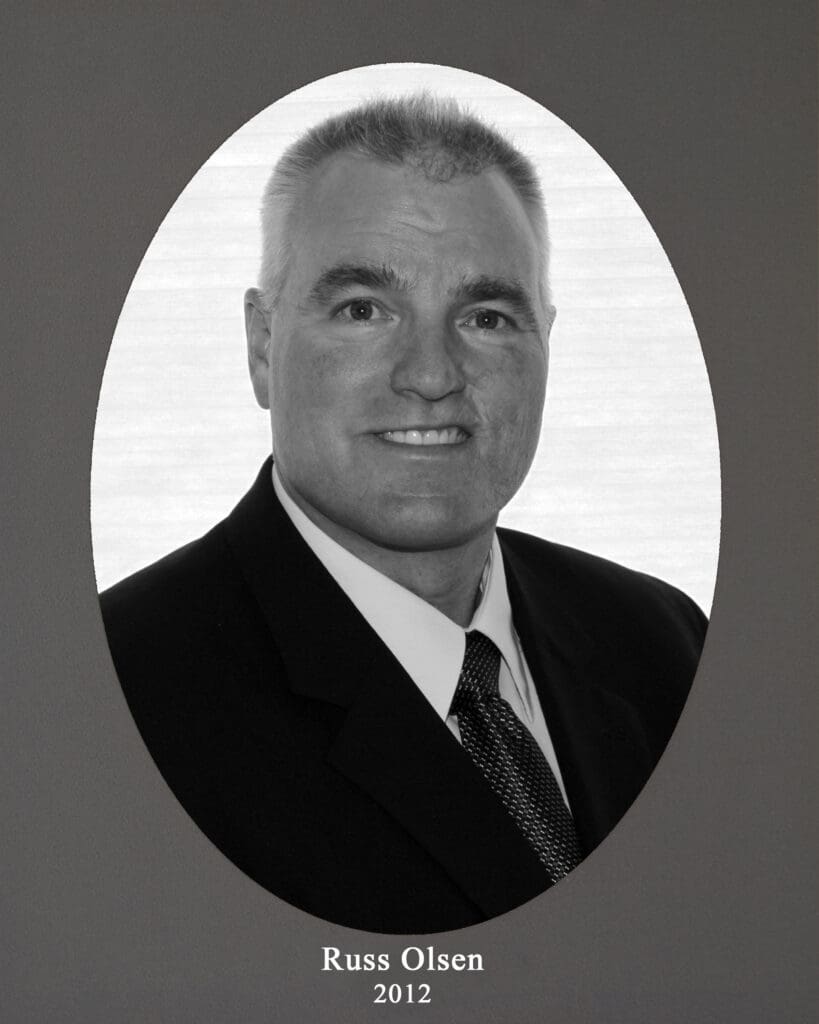 Black-and-white portrait of a man in a suit, framed by a white oval on a gray background, captioned 'Russ Olsen 2012'.