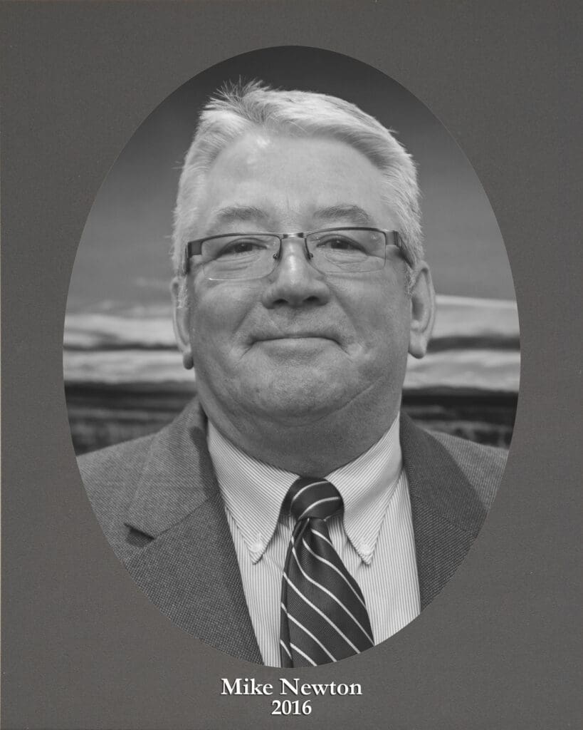 Black-and-white portrait of a smiling man with gray hair and glasses in a suit and striped tie, against a gray backdrop with the text 'Mike Newton 2016' at the bottom.