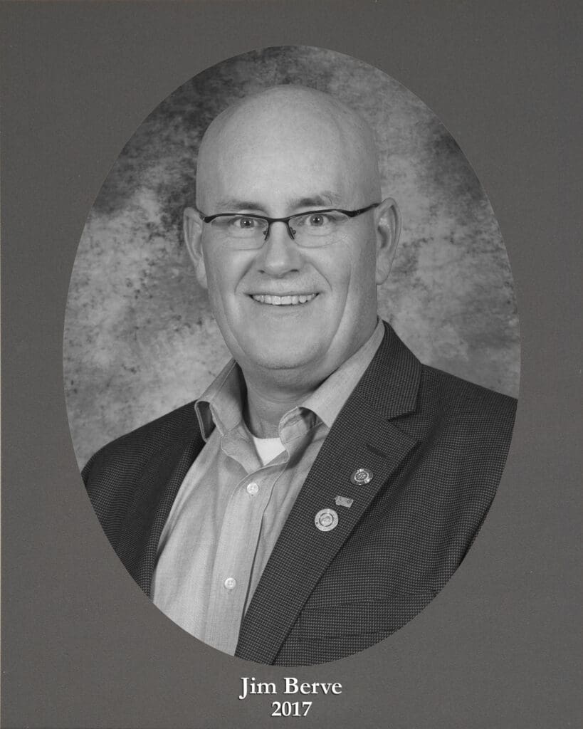 Black-and-white head-and-shoulders portrait of Jim Berve in a suit, smiling, with a circular frame and'Jim Berve 2017' caption below