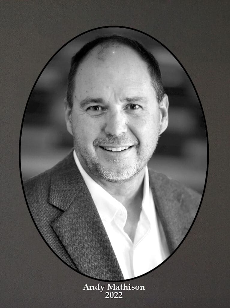 Black-and-white portrait of a smiling man in a suit, framed in an oval on a dark background; caption reads'Andy Mathison 2022'.