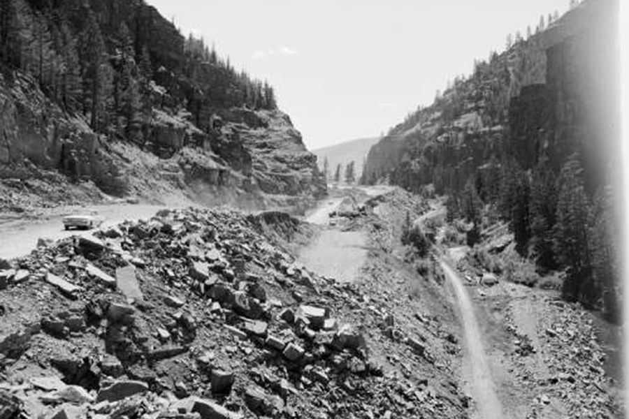 Mountain pass blocked by a large rockslide; a vehicle appears in the distance for scale as rubble covers the road.