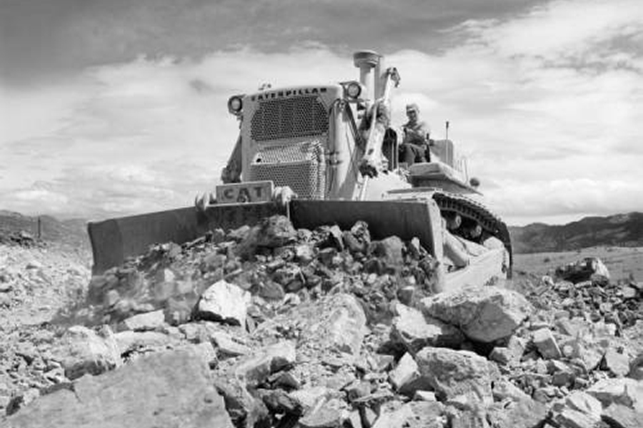 Caterpillar bulldozer pushing a rock pile in a quarry under a cloudy sky.